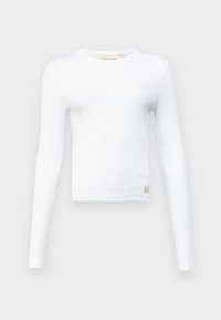 Maglietta bianca a maniche lunghe realizzata in tessuto a costine con scollatura rotonda. Presenta una piccola etichetta con logo all'orlo. Silhouette semplice e aderente.