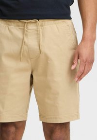 Beige cotton shorts with an elastic waistband and drawstring. Features side pockets and a relaxed fit, with a smooth texture.