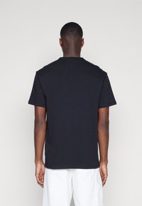 Czarna, krótka koszulka z okrągłym dekoltem i luźnym krojem. Gładki bawełniany materiał o jednolitym wzorze, widziana od tyłu.