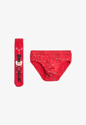 Bajo de algodón rojo con un estampado de cascanueces y una cinturilla que dice "XMAS", combinado con medias rojas hasta la rodilla que presentan un diseño de cascanueces y el texto "HO HO HO".