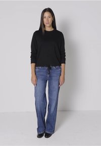 Suéter negro de manga larga combinado con jeans de pierna ancha azules. El suéter tiene un ajuste relajado; los jeans presentan una textura de denim clásica y una cuerda en la cintura.