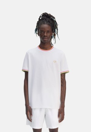 Camiseta blanca de manga corta con cuello redondo, con rayas rojas, verdes y amarillas. Logo bordado en dorado en el pecho. Textura suave.