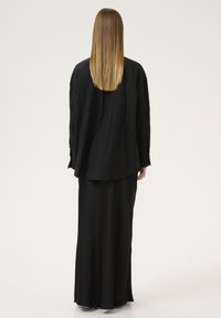 Czarna, oversized koszula o fakturowanej tkaninie, z długimi rękawami i luźnym krojem, zestawiona z „zwiewną” czarną spódnicą. Prosty design, bez ozdób.