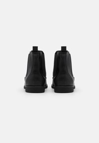 Bottines en cuir noir avec panneaux latéraux élastiques et languettes pour les enfiler, dotées d'une semelle en caoutchouc noir texturée et d'un design lisse et épuré.