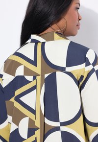 Camicia con colletto caratterizzata da un motivo geometrico nei colori blu navy, bianco e verde oliva. Realizzata in tessuto morbido con una vestibilità rilassata e dettagli di pieghe laterali.