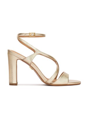 Arany színű, vastag sarokkal rendelkező magassarkú szandál, átlapolt pántokkal és bokapántos csattal, oldalnézetben.