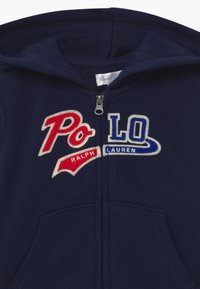 Felpa con cappuccio blu navy caratterizzata dal logo "Polo" ricamato in rosso e blu, con chiusura a zip e tasche frontali. Tessuto morbido.