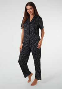 Czarny zestaw piżamy z krótkimi rękawami i długimi spodniami, ozdobiony małymi białymi wzorami w serca. Wykonany z gładkiego, lekkiego materiału.