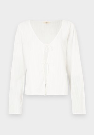 Bela dolga bluza z dolgimi rokavi, globokim V-izrezom, detajlom z zavezovanjem spredaj ter teksturiranimi črtami po celotnem tkanju.