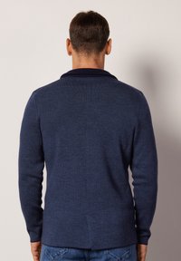 Marineblauer Strickcardigan mit einem Schalkragen, taillierter Passform und langen Ärmeln. Mit einer Rückennaht und einem seitlichen Schlitz am Saum.