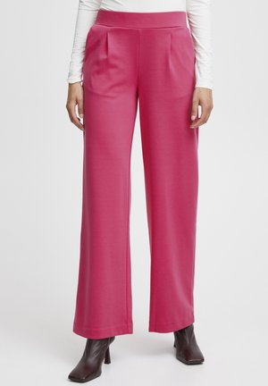 Pantaloni a gamba larga pink con vita alta, caratterizzati da pieghe sul davanti. Realizzati in un tessuto morbido e elasticizzato. Indossati con stivali neri con tacco.