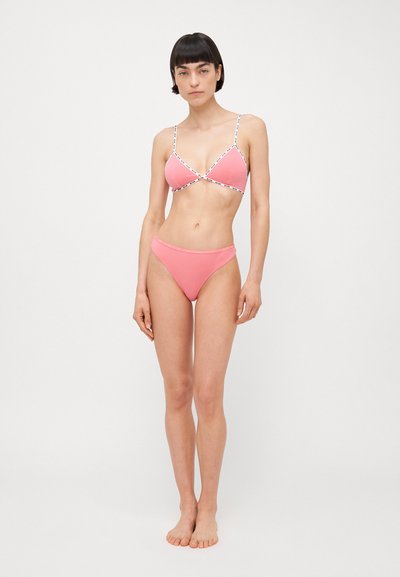 Rozā bikini ar trīsstūra augšdaļu, kuram ir baltas siksnas un mezglu detaļa. Gluda tekstūra, minimālisma dizains un klasiskas zemas jostasvietas apakšdaļa.