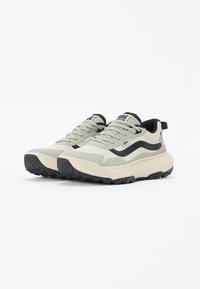 Lys grå og kremfargede lave sneakers med svarte detaljer, teksturert gummisåle og kontrasterende stripe-design. Klassisk snøring.