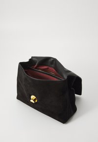 Svart mockaväska med ett guld cirkulärt spänne, med ett zip-fodral i burgundytyg och mjukt läderkant upptill.