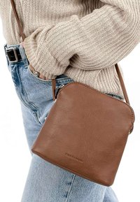 Sac bandoulière en cuir marron avec une texture lisse, de forme carrée et avec une fermeture éclair. Équipé d'une fine bandoulière et d'un logo embossé.