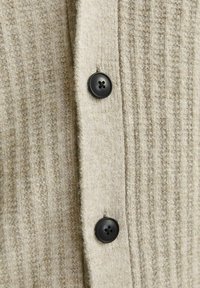 Beiger, gerippter Cardigan aus strukturiertem Strickstoff, mit schwarzen Knöpfen und einem weichen Finish. Das Design umfasst vertikale Streifen.