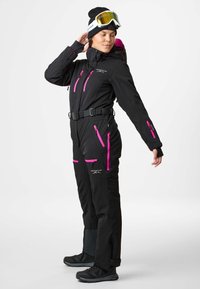 Black ski suit featuring pink zippers and accents, a belted waist, multiple pockets, and a fitted design. Suitable for winter activities.