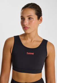 Svart sport-bh i mjukt, stretchigt material. Har rundad halsringning, breda axelband och en röd "hummel PERFORMANCE"-logotyp i mitten.