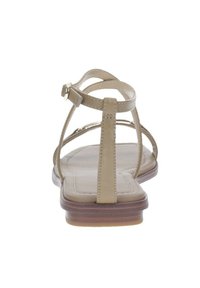 Sandali piatti beige dal design minimalista, caratterizzati da sottili cinturini, una silhouette a t-strap e una suola testurizzata con un leggero tacco rialzato.