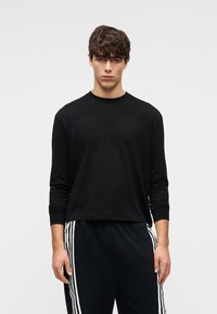 Μαύρο μακρυμάνικο μπλουζάκι από απαλό βαμβάκι, με στρογγυλή λαιμόκοψη και εφαρμοστά μανίκια, συνδυασμένο με μαύρη φόρμα με λευκές ρίγες στα πλαϊνά.