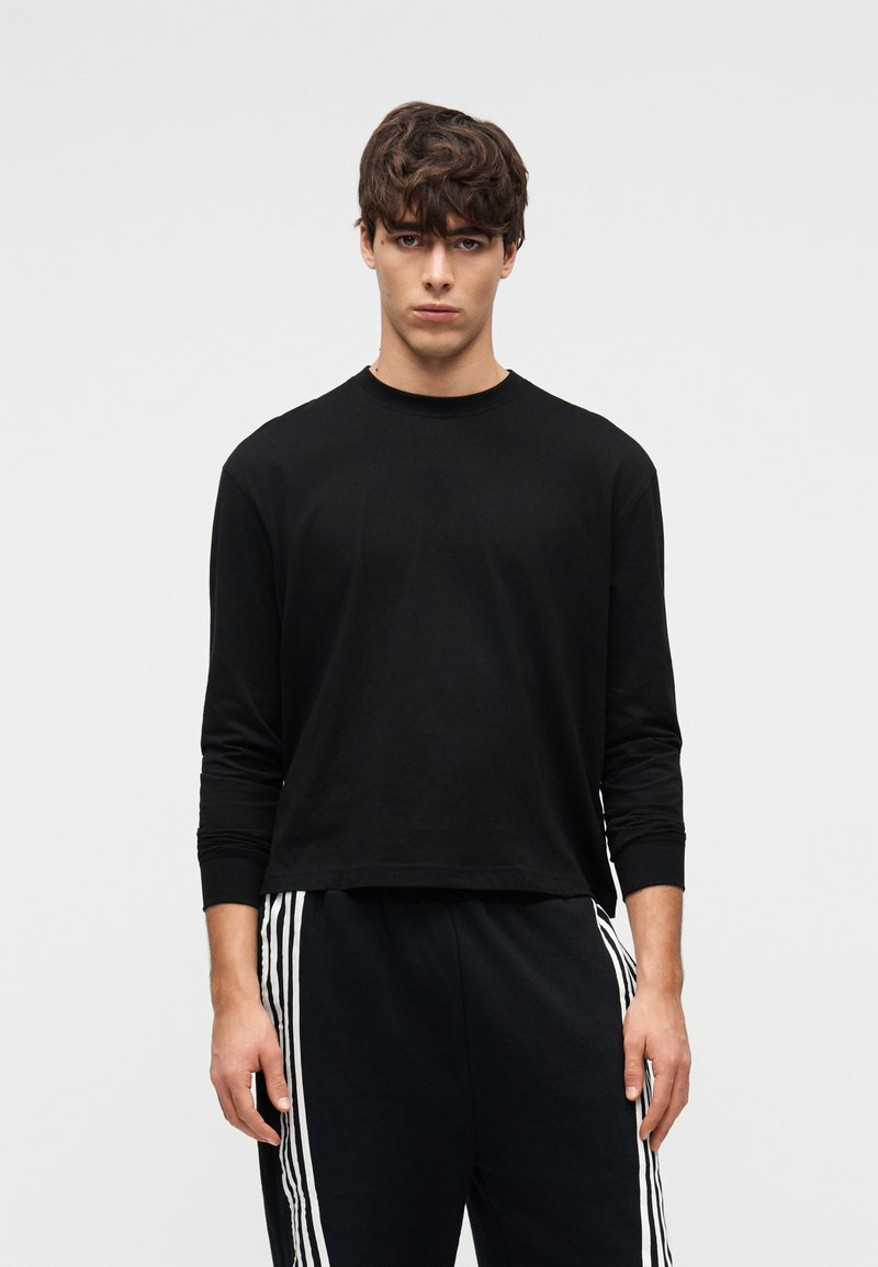 Μαύρο μακρυμάνικο μπλουζάκι από απαλό βαμβάκι, με στρογγυλή λαιμόκοψη και εφαρμοστά μανίκια, συνδυασμένο με μαύρη φόρμα με λευκές ρίγες στα πλαϊνά.