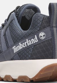 Tmavě modré tenisky Timberland s texturovaným textilním svrškem, bočním panelem s logem a gumovou podrážkou s charakteristickým vzorem.