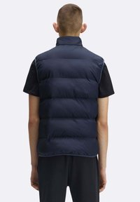 Smanicato imbottito blu navy con collo alto, caratterizzato da sezioni trapuntate orizzontali e una texture liscia, indossato sopra una maglietta nera a maniche corte.