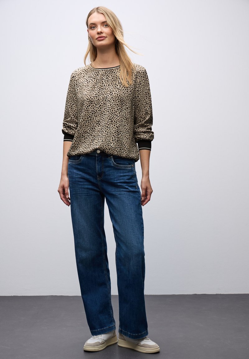 Maglione con stampa leopardata e bordo nero, abbinato a jeans in denim blu a gamba larga e scarpe sportive bianche. Tessuti morbidi e vestibilità casual.