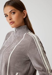 Grijze zip-up top met hoge kraag, voorzien van witte strepen op de mouwen en een zachte, gemêleerde stof. Aangevuld met een half-rits sluiting.