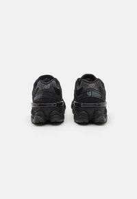 Baskets de sport noires avec un tissu texturé, une semelle rembourrée et des accents brillants. Présente une forme arrondie et un logo sur le talon.