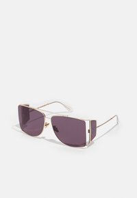 Occhiali da sole con lenti viola grandi e una forma geometrica. Aste in metallo dorato con punte trasparenti e dettagli laterali.