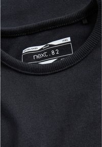 Sort bomuldscrew neck sweatshirt med ribbet halsudskæring, prydet med en hvid label, der viser "next. 82" og branddetaljer. Glat tekstur.