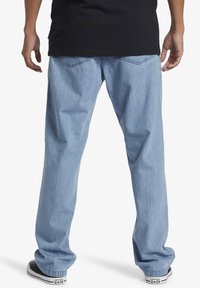 Svijetloplave traperice opuštenog kroja, s stražnjim džepovima i suptilnim detaljima šivanja. Nosene s crnim tenisicama i crnom majicom.