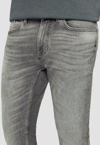 Graue Denim-Jeans mit einer figurbetonten Passform, dezentem Verblassen und klassischer Fünf-Taschen-Styles. Das Material hat eine glatte, leicht strukturierte Oberfläche.