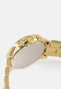 Orologio in tonalità oro con cassa rotonda, bezel texturizzato e tre pulsanti di controllo. Bracciale a stile con segmenti collegati.