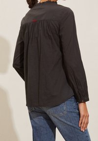 Svart långärmad tröja med samlad halsringning och röd sömdetalj på baksidan, i kombination med blå denimjeans. Mjuk tygtextur.