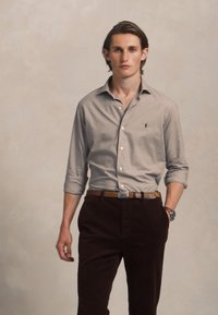 Lys grå skjorte med lange ermer, kombinert med brune kordfløyelsbukser og et brunt belte. Slim fit, klassisk krage, uten mønstre.