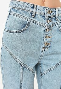 Světle modré džíny z denimu s vysokým pasem, zapínáním na pět knoflíků, �šikmými kapsami a horizontálními prošitím.