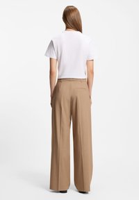 Λευκό t-shirt με κοντά μανίκια συνδυασμένο με ανοιχτό καφέ παντελόνι φαρδιάς γραμμής. Το παντελόνι διαθέτει τσέπη στο πίσω μέρος και λείο υφή.