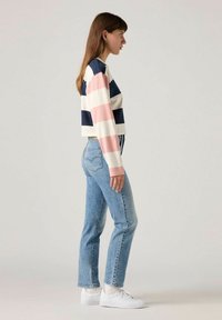 Top de manga larga a rayas en azul marino, rosa y blanco; diseño corto. Combinado con jeans rectos de tiro medio en azul claro y zapatillas blancas.