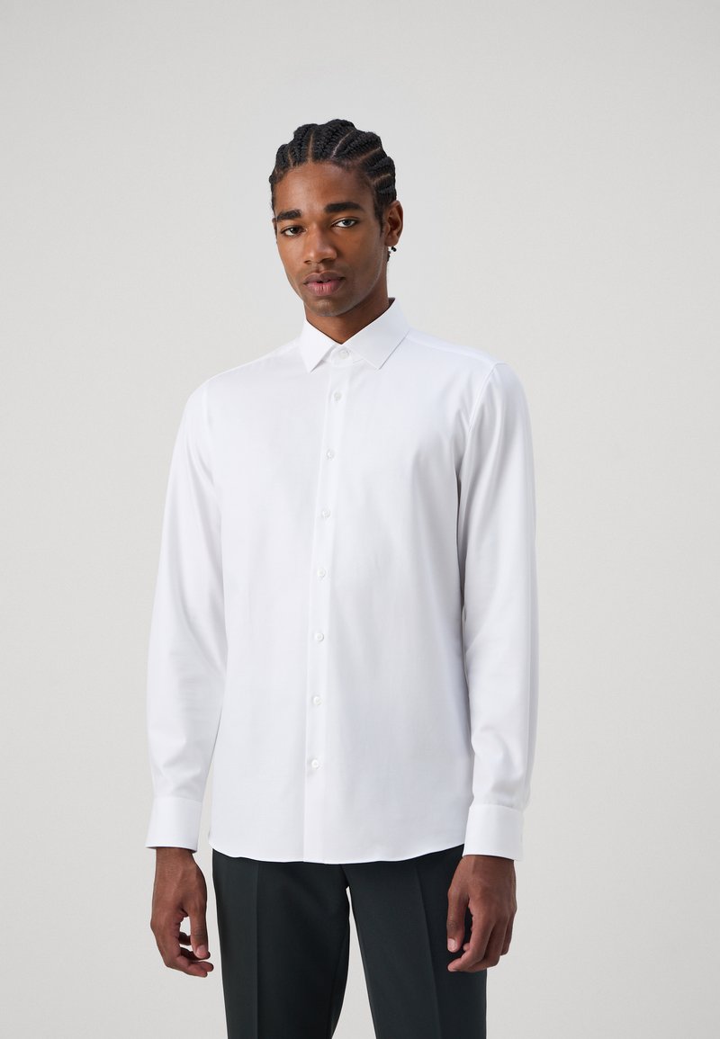 Long-sleeve white shirt with a button-up front, pointed collar, and smooth texture. Model wears with dark pants.