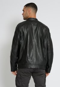 Schwarze Lederjacke mit hohem Kragen, glatter Textur und dezenten Nähdetails. Über grauen Cargo-Hosen getragen, von hinten gesehen.