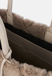 Beige handbag with faux fur trim, soft texture, and leather accents. Features sturdy handles and an interior with a logo and dark lining.