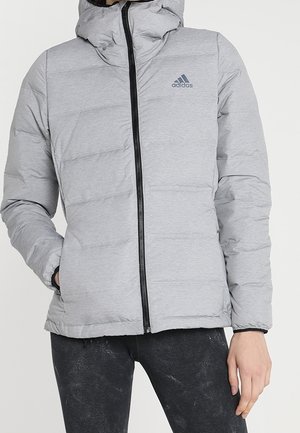 Vaaleanharmaa toppatakki, jossa hupullinen, musta vetoketju edessä ja vasemman rinnan logolla, yllään mustat housut.