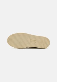 Sole di scarpa in gomma di colore beige chiaro con righe orizzontali e impronta circolare del logo. Design semplice, struttura piatta e senza motivi o dettagli visibili.
