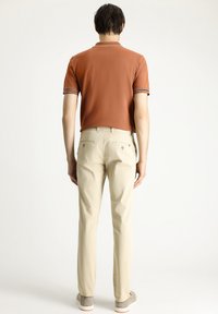 Polo naranja oscuro con cuello a rayas blancas y negras, combinado con pantalones beige de pierna recta que tienen doble bolsillo trasero.