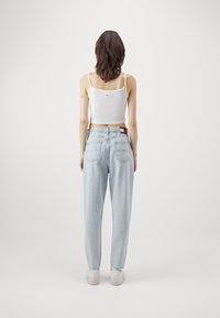 Ljust blå högmidjade jeans med en avslappnad passform, med bakfickor och en logotypetikett, kombinerat med en vit åtsittande linne och vita sneakers.