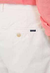 Pantaloni di cotone bianchi con una tasca posteriore dotata di chiusura a bottone e una piccola etichetta blu con la scritta "HACKETT". Design semplice e classico.