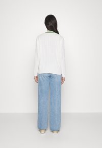 Weißer Pullover aus Kabelstrick mit einem grünen Akzentkragen, kombiniert mit lockeren hellblauen Jeans und hellen Sneakers.