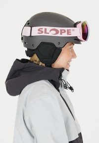 Musta hiihtokypärä, jossa on vaaleanpunainen "SLOPE"-remmi ja peilipintaiset suojalasit. Varustettu korvasuojilla ja säädettävällä leuanremmillä. Sileä matta pinta.